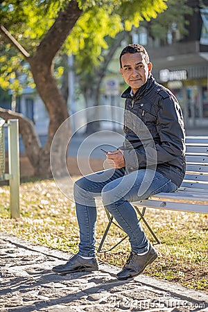 Young latin man sitting on a square bench Stock Photo