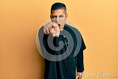 Young latin priest man standing over yellow background pointing displeased and frustrated to the camera, angry and furious with Stock Photo