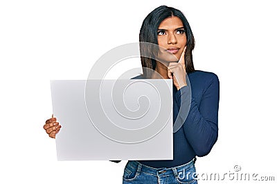 Young latin transsexual transgender woman holding blank empty banner serious face thinking about question with hand on chin, Stock Photo