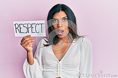 Young latin transsexual transgender woman holding respect message paper scared and amazed with open mouth for surprise, disbelief Stock Photo