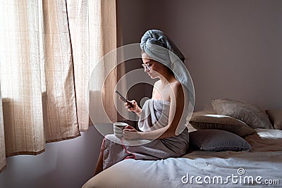 Young latin woman freshly bathed with mobile phone and coffee at home Stock Photo