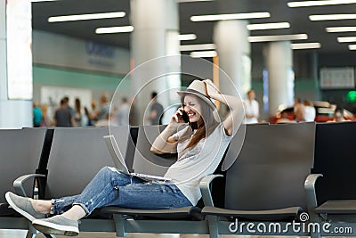 Young laughing traveler tourist woman working on laptop, talk on mobile phone, call friend, booking taxi hotel wait in Stock Photo