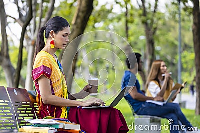 Young LGBTQ+ Asian student enjoy having relaxing time in the university campus park while sitting and studying on the bench during Stock Photo