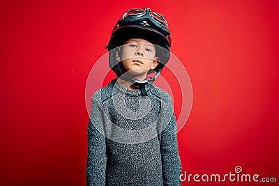 Young little caucasian kid wearing vintage biker motorcycle helmet and googles over red background with serious expression on face Stock Photo