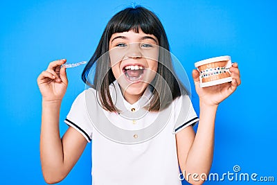 Young little girl with bang holding invisible aligner orthodontic and braces smiling and laughing hard out loud because funny Stock Photo