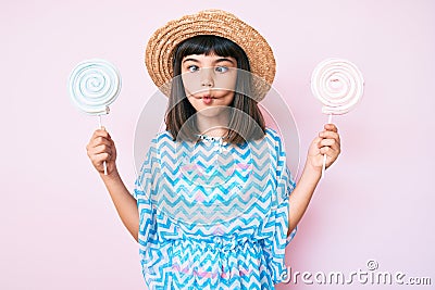 Young little girl with bang wearing summer dress eating candy making fish face with mouth and squinting eyes, crazy and comical Stock Photo