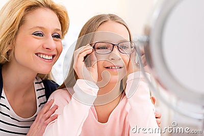 Young little girl trying glasses at the optician w her mother Stock Photo