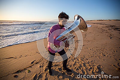 Young lone musician with a tuba playing on the sea beach Stock Photo