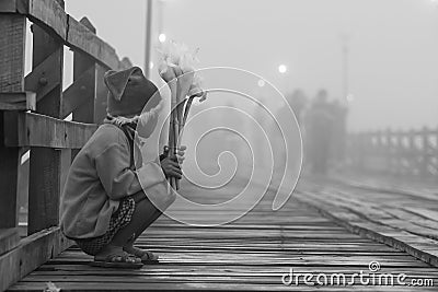 Young lonely poor boy selling flowers at Mon wooden bridge in cold morning Editorial Stock Photo