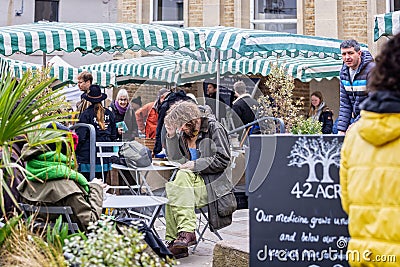 Young long haired and bearded man sat reading book at outdoor cafe at Frome Sunday Market, Somerset, UK Editorial Stock Photo