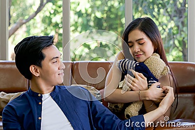 Young lovers spend time together on holidays in the living room. The young man wears comfortable clothes, hand a teddy bear to Stock Photo