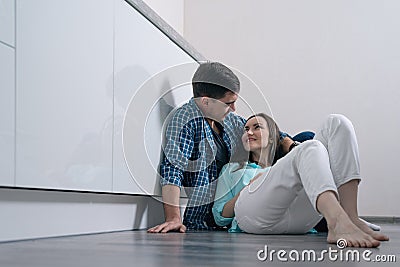 Young loving couple on the parquet floor in white kitchen interior sitting and smiling at each other Stock Photo