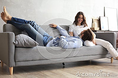 Young loving couple relaxing on sofa together, husband lying on wife legs resting on couch Stock Photo