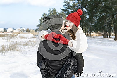 Young loving couple in winter forest. Happy young woman keeps hands in heart shape and embrace her boyfriend. Sunny day Stock Photo