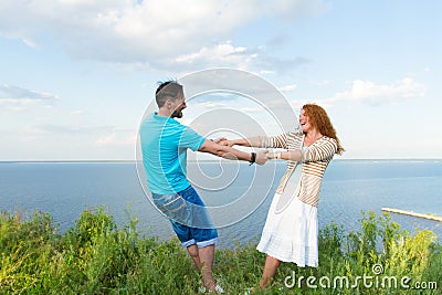 Young loving smiling couple in grass on lake and sky background. Shot of attractive young red hair woman dancing with boyfriend Stock Photo