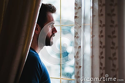 Young mad standing by the window looking outside Stock Photo