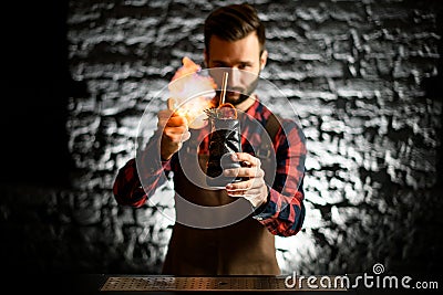 Young male bartender holds black ceramic glass with slice of citrus and make fire Stock Photo