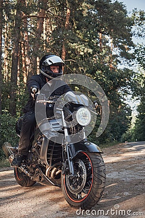 Young male biker in a helmet travels on a motorcycle alone, on a road in the forest Stock Photo