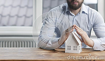 A young male businessman holds his hands over a miniature paper house. The concept of protection and security of property and home Stock Photo