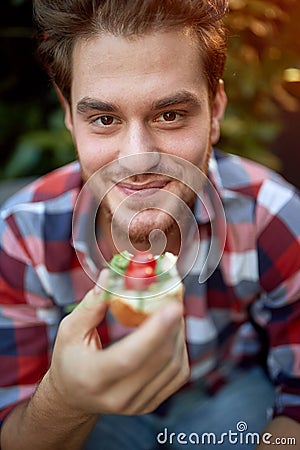 Young male caucasian holding sandwich that is about to eat, looking at camera, smiling Stock Photo