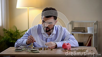 Young male counting coins, piggy bank standing by, financial literacy, budget Stock Photo