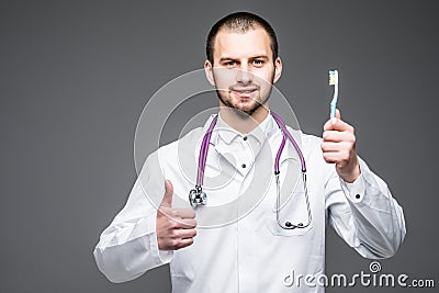 Young male dentist or stomatologist holding toothbrush isolated on gray background Stock Photo