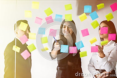 Young male and female coworkers writing remaining notes for colleagues planning productive working process in office. Smiling stud Stock Photo