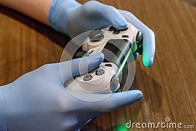 Young male hands in medical gloves handing play station remote over the table and playing game. Home staying. Social safe Editorial Stock Photo