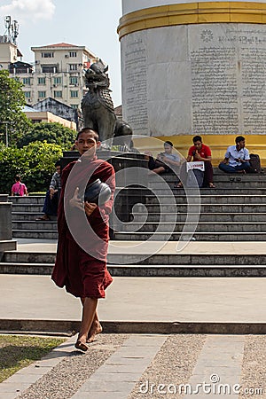 Young male monk asking for alms, food or money. Dressed in traditional red clothes, shaved head. Carrying alm bowl. Walking Editorial Stock Photo