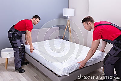 Young Male Movers Placing The Mattress Over The Bed Stock Photo