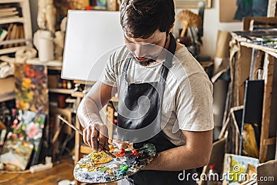 Male painter at art studio indoors mixing colors on palette with brush concentrated Stock Photo