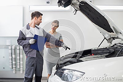 Young male repairman explaining car engine to female customer in automobile repair shop Stock Photo