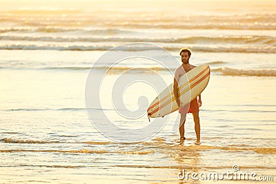 Young male surfer at the beach for sunrise with surfboard Stock Photo