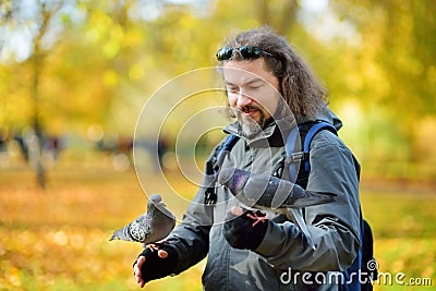 Young male tourist feeding pigeons in St James`s Park in London, United Kingdom, on beautiful sunny autumn day Stock Photo