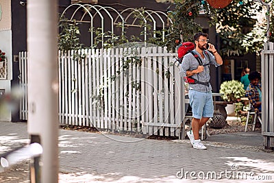 Young male tourist talking on a smartphone in front of the hostel. Travel, tourism and people concept Stock Photo