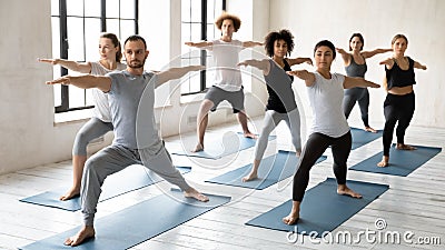 Young male trainer leading yoga class for concentrated multiracial students. Stock Photo