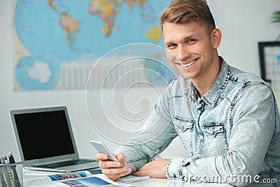 Young male travel agent consultant in tour agency holding smartphone Stock Photo