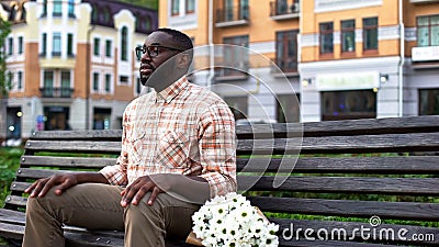 Young male waiting for woman, sitting on park bench with flowers, blind date Stock Photo