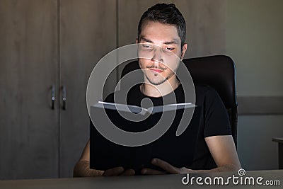 Young man or an adult guy in the dark reads a glowing book. The concept of teaching is light, not teaching is darkness Stock Photo