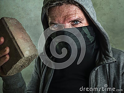 Young man as fanatic and aggressive anarchist rioter . furious and scary violent anti-system protester in face mask throwing brick Stock Photo