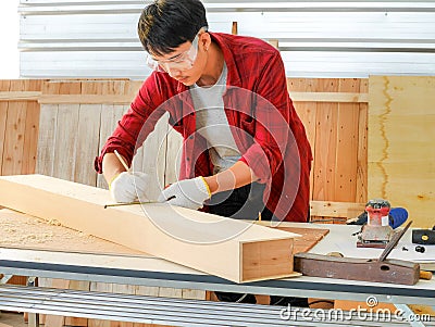 Young man Asian carpenter with red shirt in workshop store working on wood plank and measurement tools Stock Photo