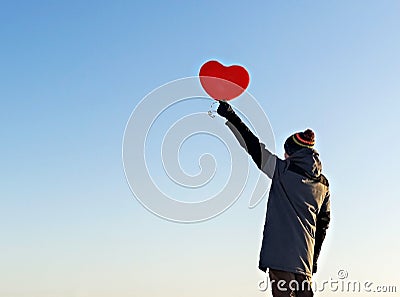 Young man from the back with a red heart-shaped balloon against the blue sky. Valentine day concept, copy space Stock Photo