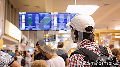 Young man with backpack checking flight information on digital schedule display inside arrival hall in international Stock Photo