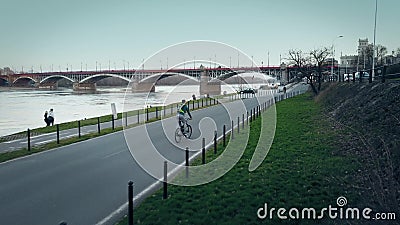 Young man with backpack riding his bike along evening river embankment Editorial Stock Photo