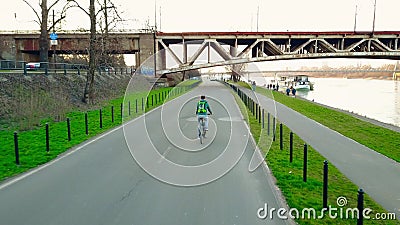 Young man with backpack riding his bike along evening river embankment Stock Photo