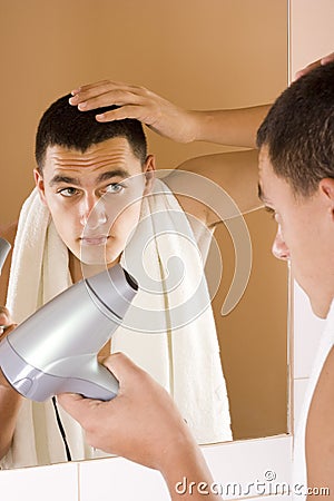 Young man in the bathroom's mirror using hair drier Stock Photo