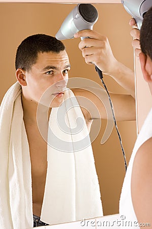 Young man in the bathroom's mirror using hair drier Stock Photo