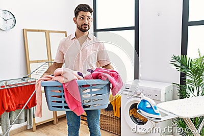 Young man with beard holding laundry basket smiling looking to the side and staring away thinking Stock Photo