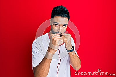 Young man with beard listening to music using headphones ready to fight with fist defense gesture, angry and upset face, afraid of Stock Photo