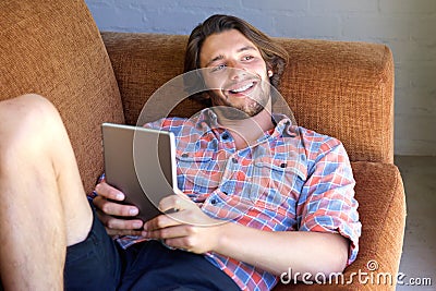 Young man with beard lying on sofa with digital tablet Stock Photo